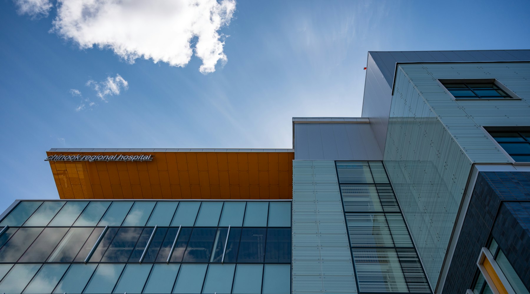 Moderne Klinikfassade aus Glas und Metall vor blauem Himmel